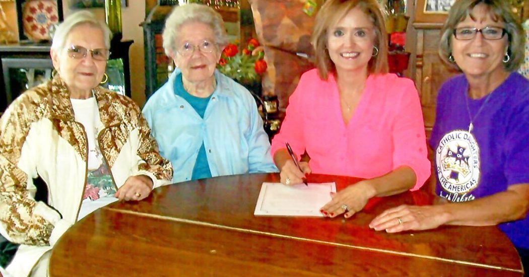 Members of Ct. Father Tracy No. 2121 Catholic Daughters of the Americas gather around Bowman City Commission President Lyn James to review the signed proclamation for CDA Sunday.